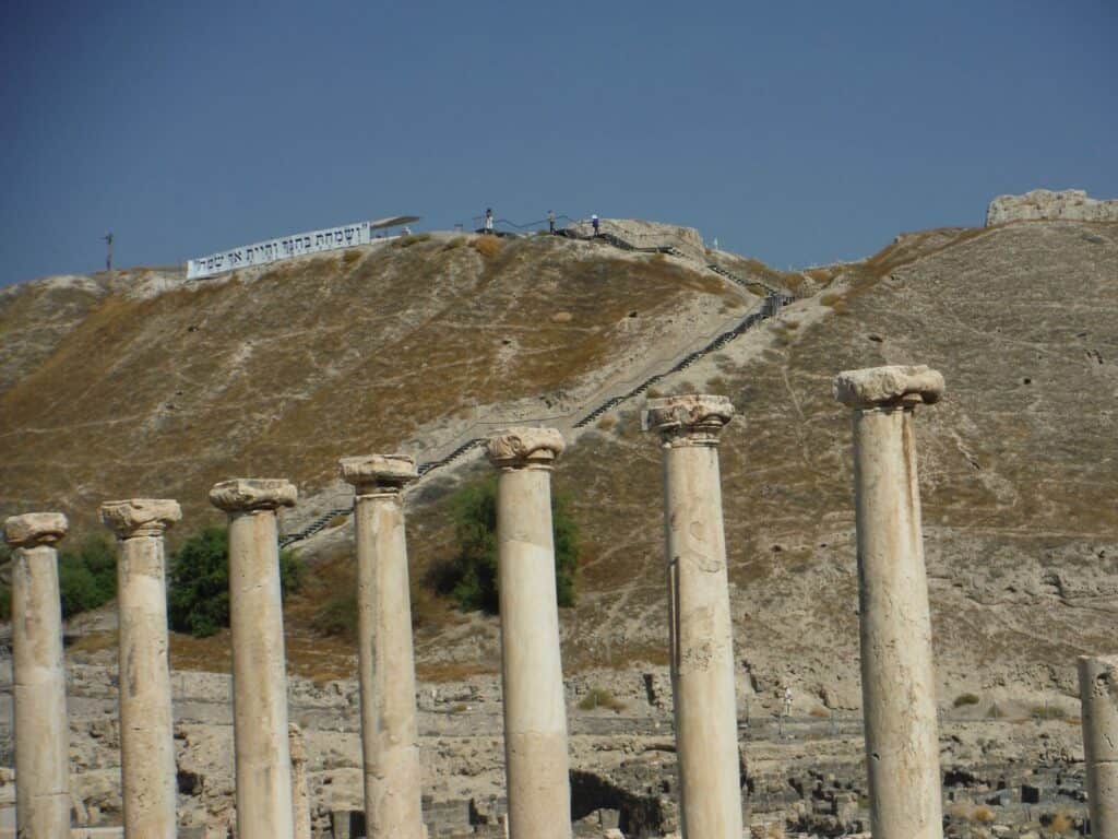 The colonnaded street at Beth Shean with the tell rising behind it, a row of columns still standing along the paved way