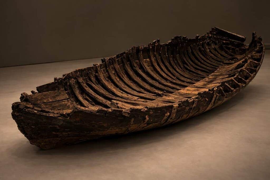 The preserved hull of the first-century Galilee boat displayed in a darkened museum gallery, its wooden ribs and planking lit from above